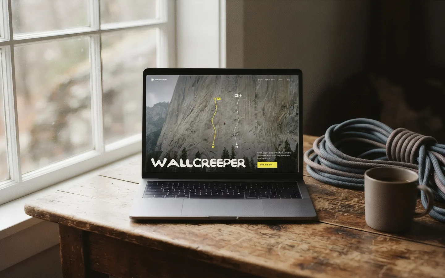 The Wallcreeper storefront open on a laptop on a wooden table by a window, next to a coiled rope and a mug.